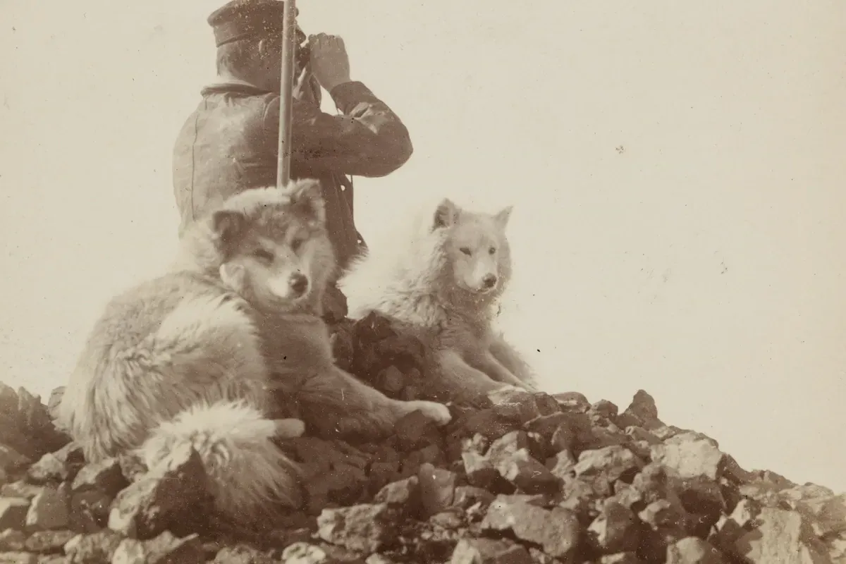 Samoyed history, two sledge dogs resting on rocks beside an explorer with binoculars, Antarctica, 1899